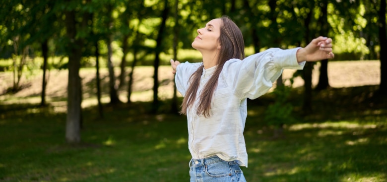 Beautiful young woman enjoy summer time in park outstretching her arms and relaxing